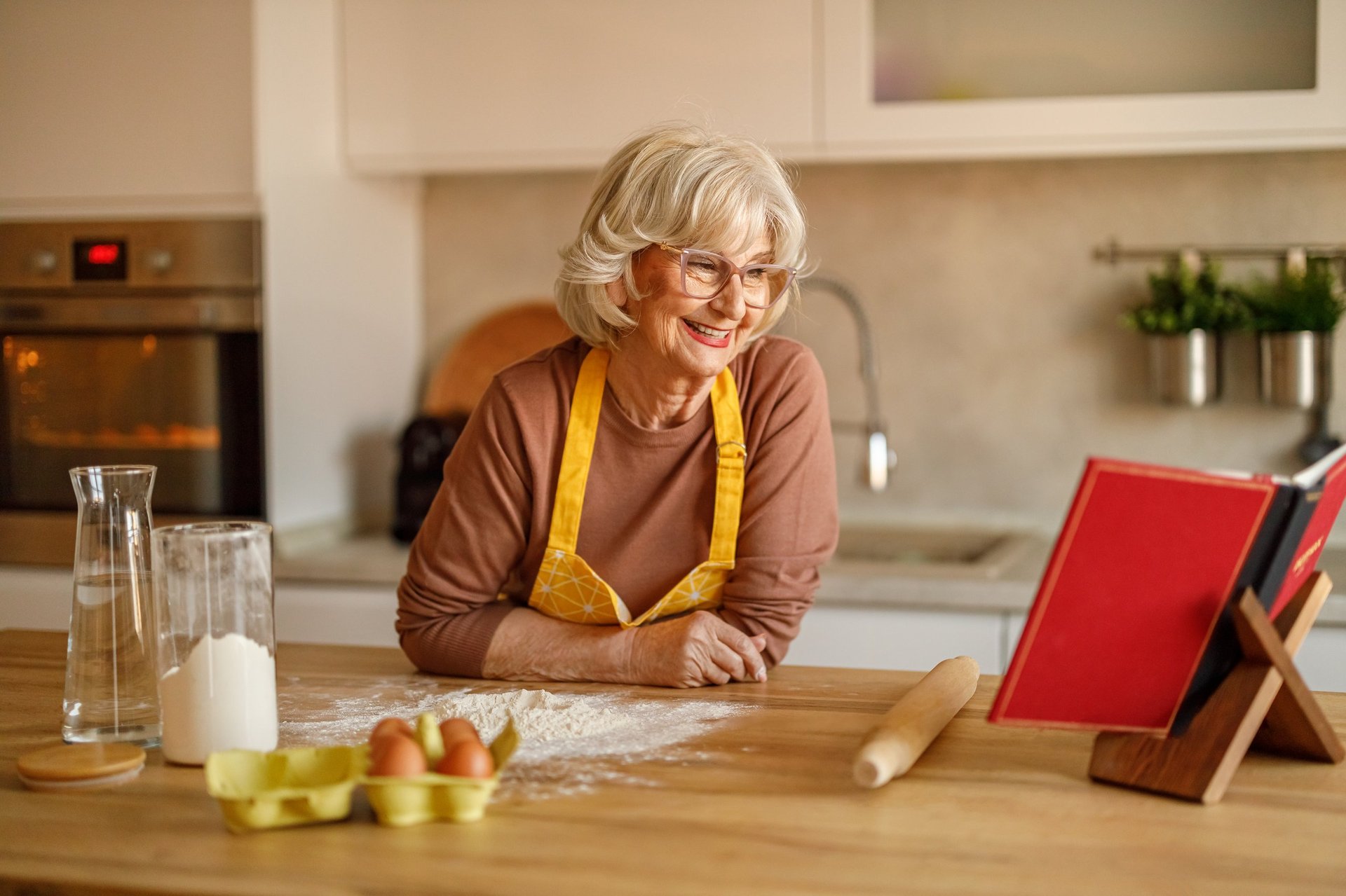 Cookbook author reading her recipes beside flour and eggs while preparing sweets for her published cookbook