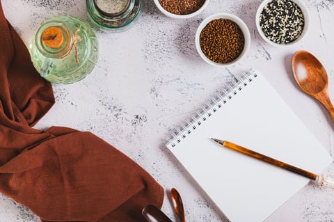 Notebook and pen for writing recipes, with spoons and spices on a kitchen table