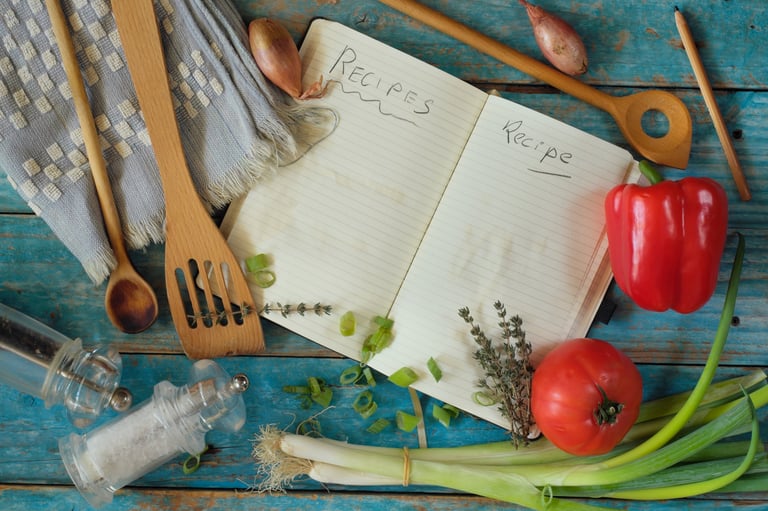 Cookbook interior spread with recipe pages surrounded by fresh vegetables and kitchen utensils